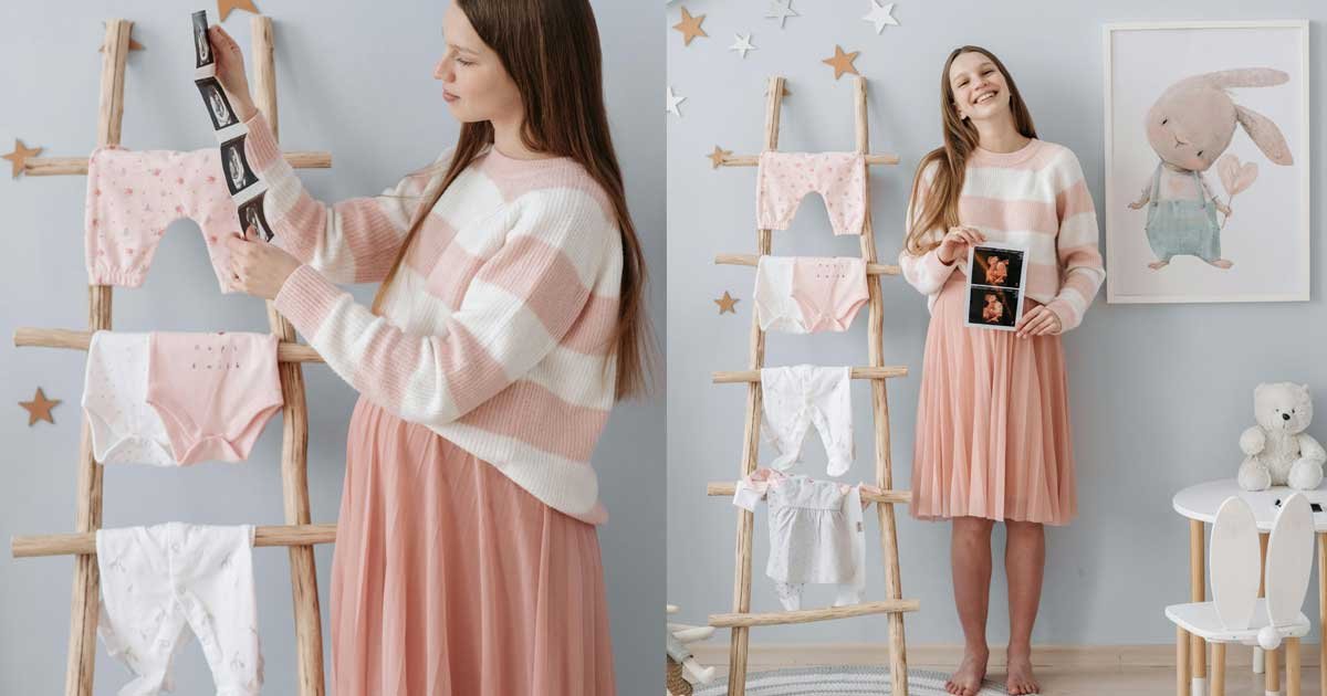 Expecting mother holding ultrasound photos while standing beside baby clothes in a nursery setting
